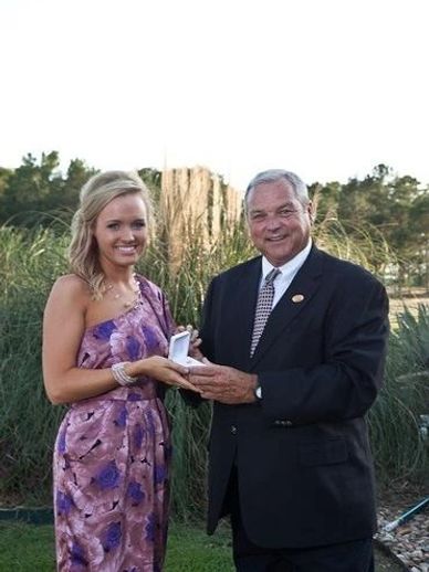 A woman in a purple dress and a man in a suit holding a small open box outdoors — Drew Henson, 2011 Yam Queen, with President Randy Hill